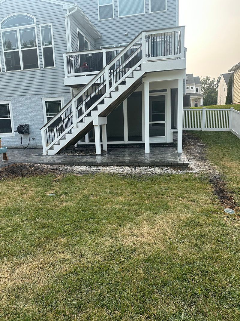 A two-story house with a white deck and stairs leading to the backyard.
