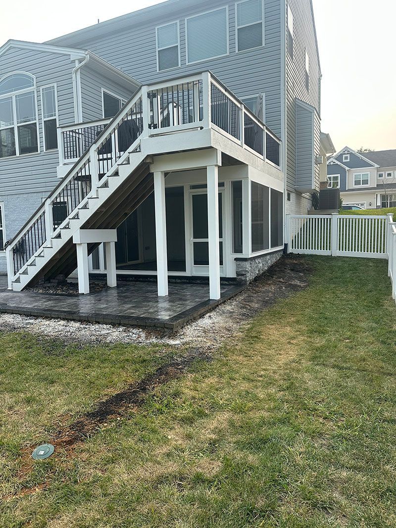A two-story house with a deck, stairs, and a screened-in porch in a grassy backyard.