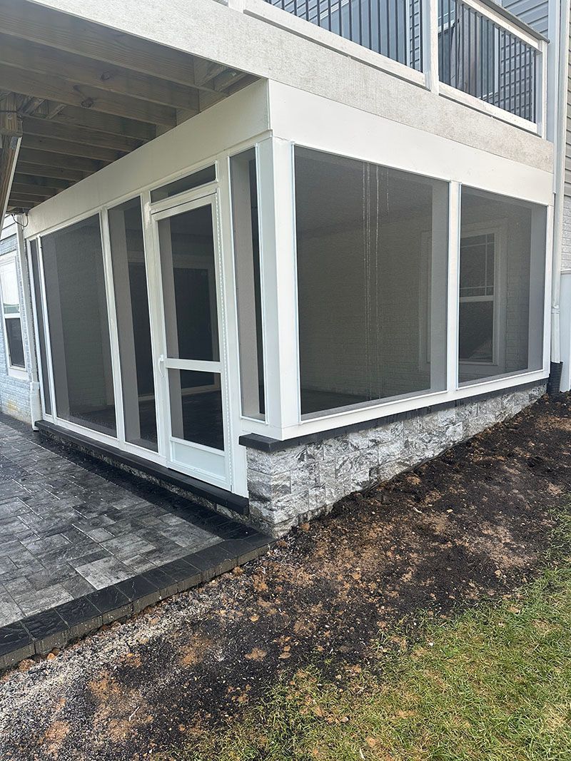 Screened-in porch with white trim, stone base, and black patio.