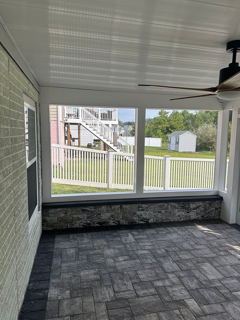 Covered patio with stone floor, white railing and ceiling, overlooking a white picket fence and yard.