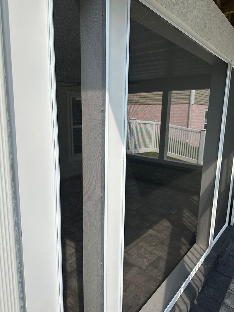 Screened porch interior with white posts and roof, looking into a room with windows and a deck.