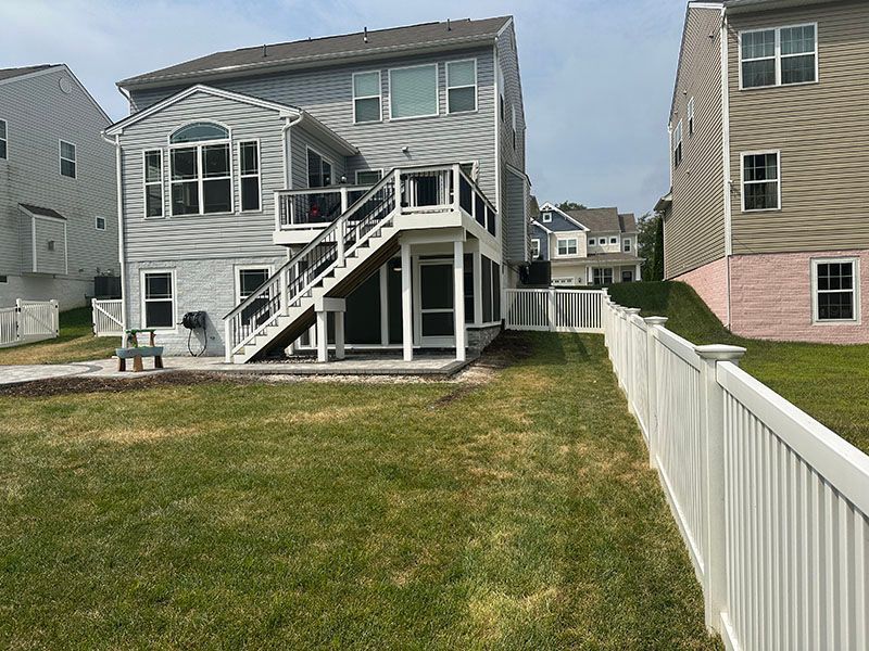 Backyard of a two-story house with a white fence and a green lawn.