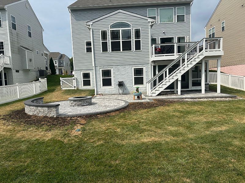 Backyard with gray house, deck, fire pit, and green lawn.
