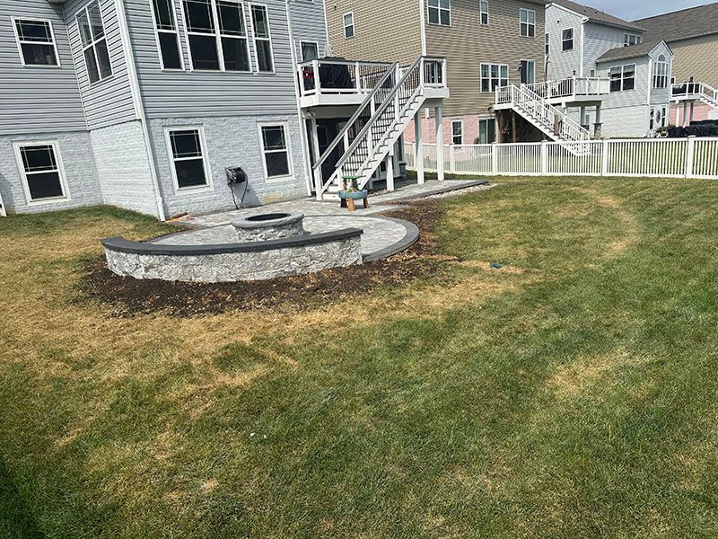 Backyard with fire pit and tiered deck. Brown and green lawn with gray houses.