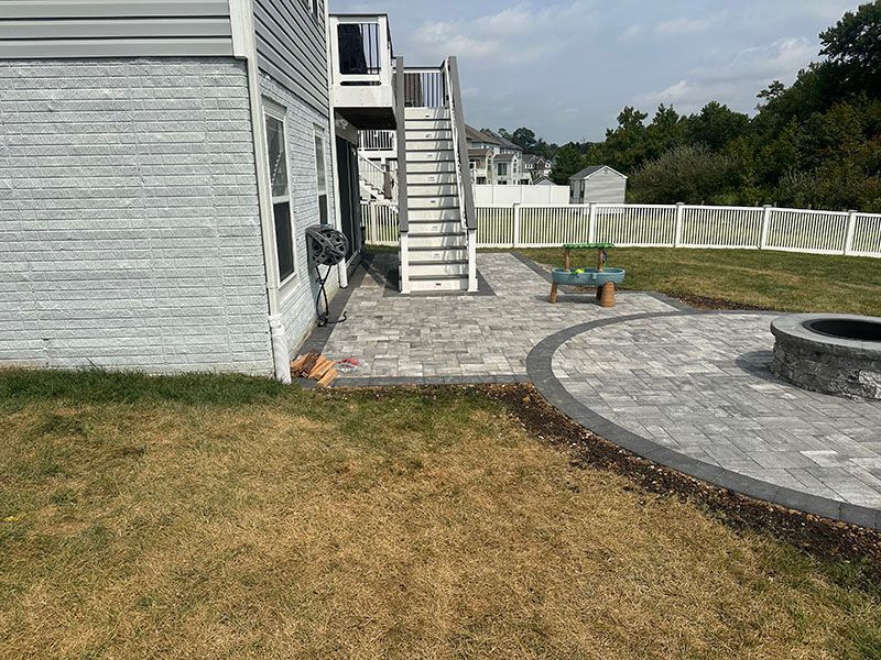 Backyard patio with gray pavers, stairs to deck, fire pit, and lawn.