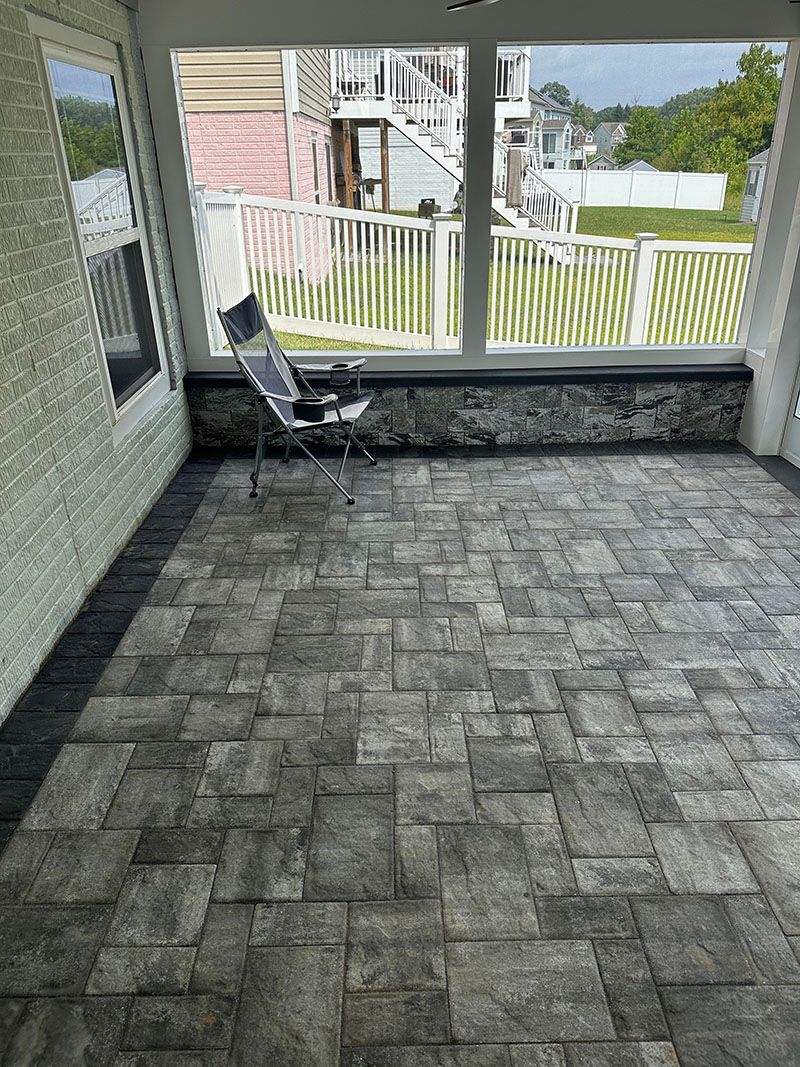 Enclosed patio with gray stone tile flooring, white trim, and view of a yard with a chair.