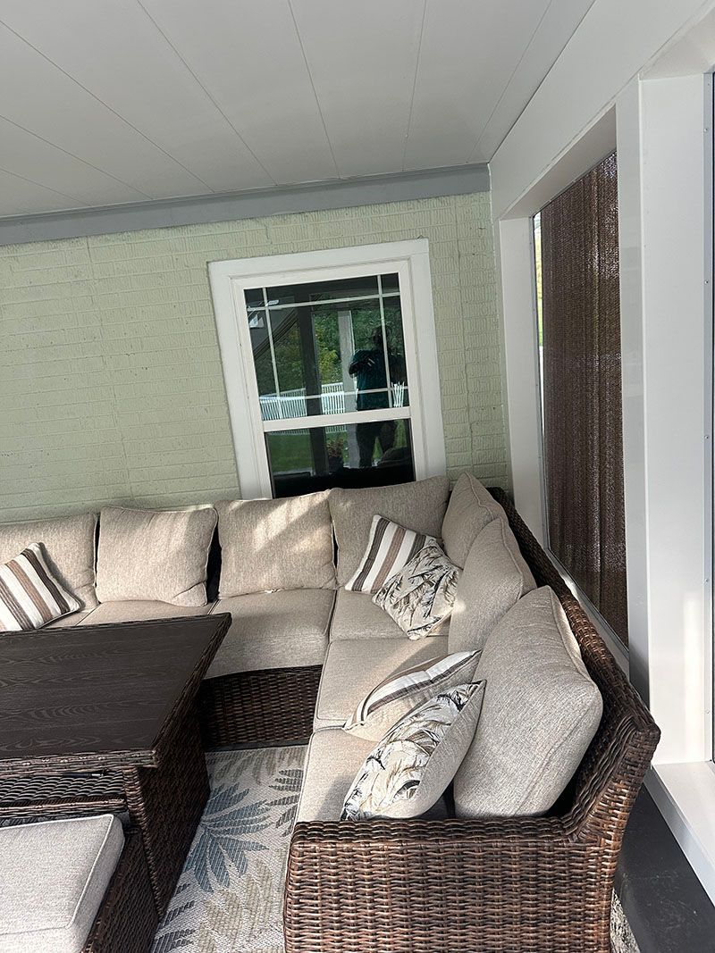 Outdoor sectional sofa with woven brown frame and beige cushions, on a porch.