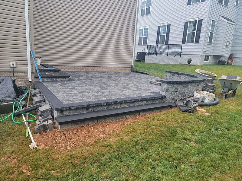 A partially built patio with steps and a curved retaining wall next to a house.