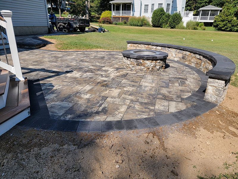 Paver patio with fire pit and low stone wall in a yard.