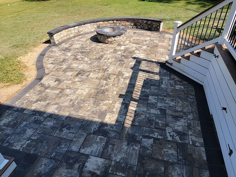 Stone patio with a fire pit and seating area, next to a white deck with black railing.