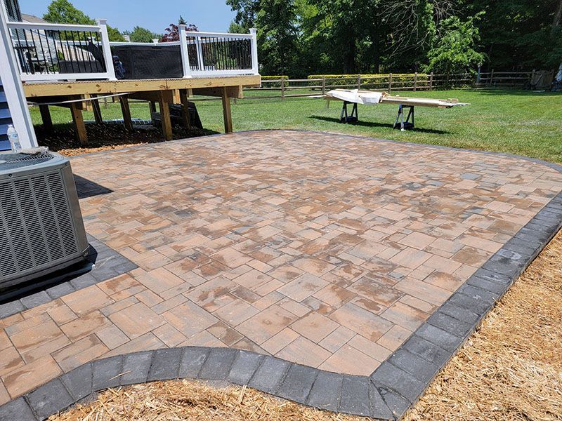 Brick patio with a dark gray border, air conditioner, and wooden deck.