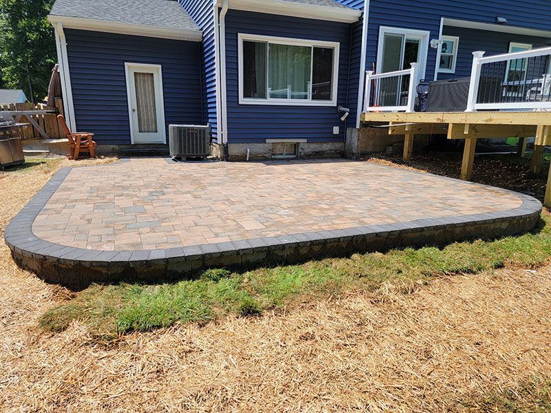 A brick patio with a low wall next to a blue house and deck, surrounded by grass.