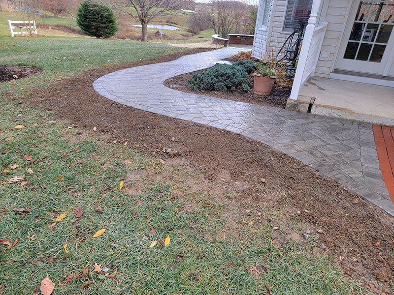 A curving gray paver walkway leads to a house with a white exterior.
