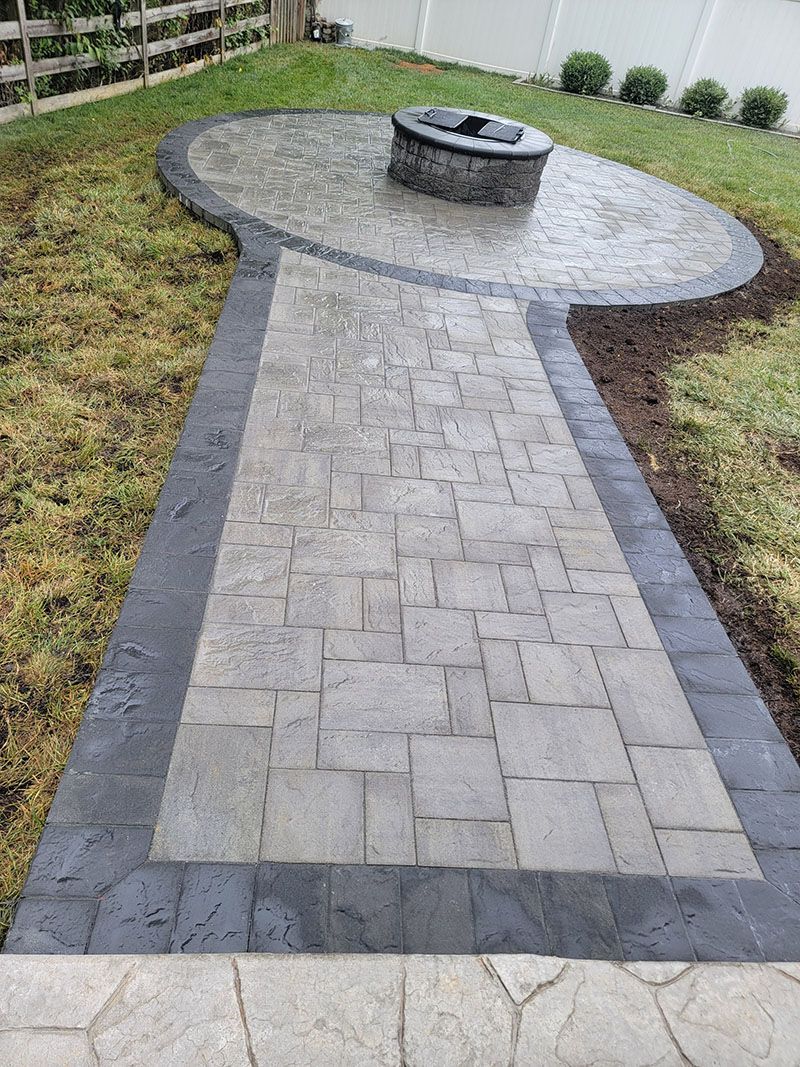 Patio with a fire pit and a pathway of concrete pavers surrounded by grass.