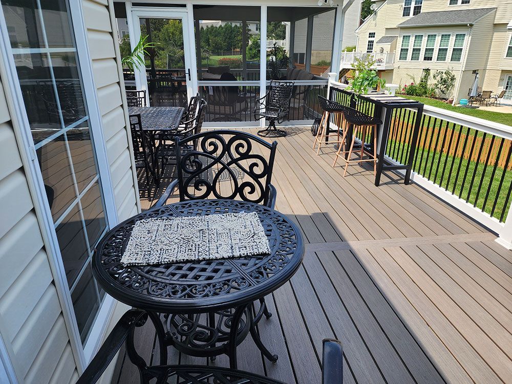 A wrought-iron table and chairs on a composite deck, with a screened porch and residential background.