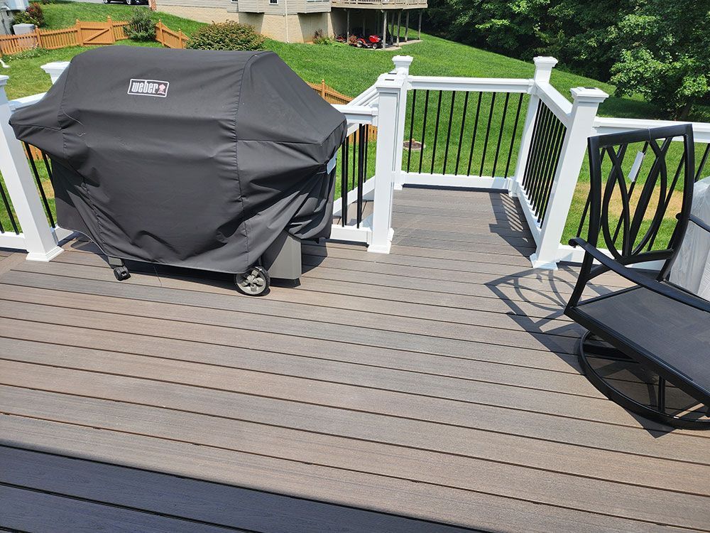 Deck with a grill, chair, and railing. Wooden deck and green yard in the background.