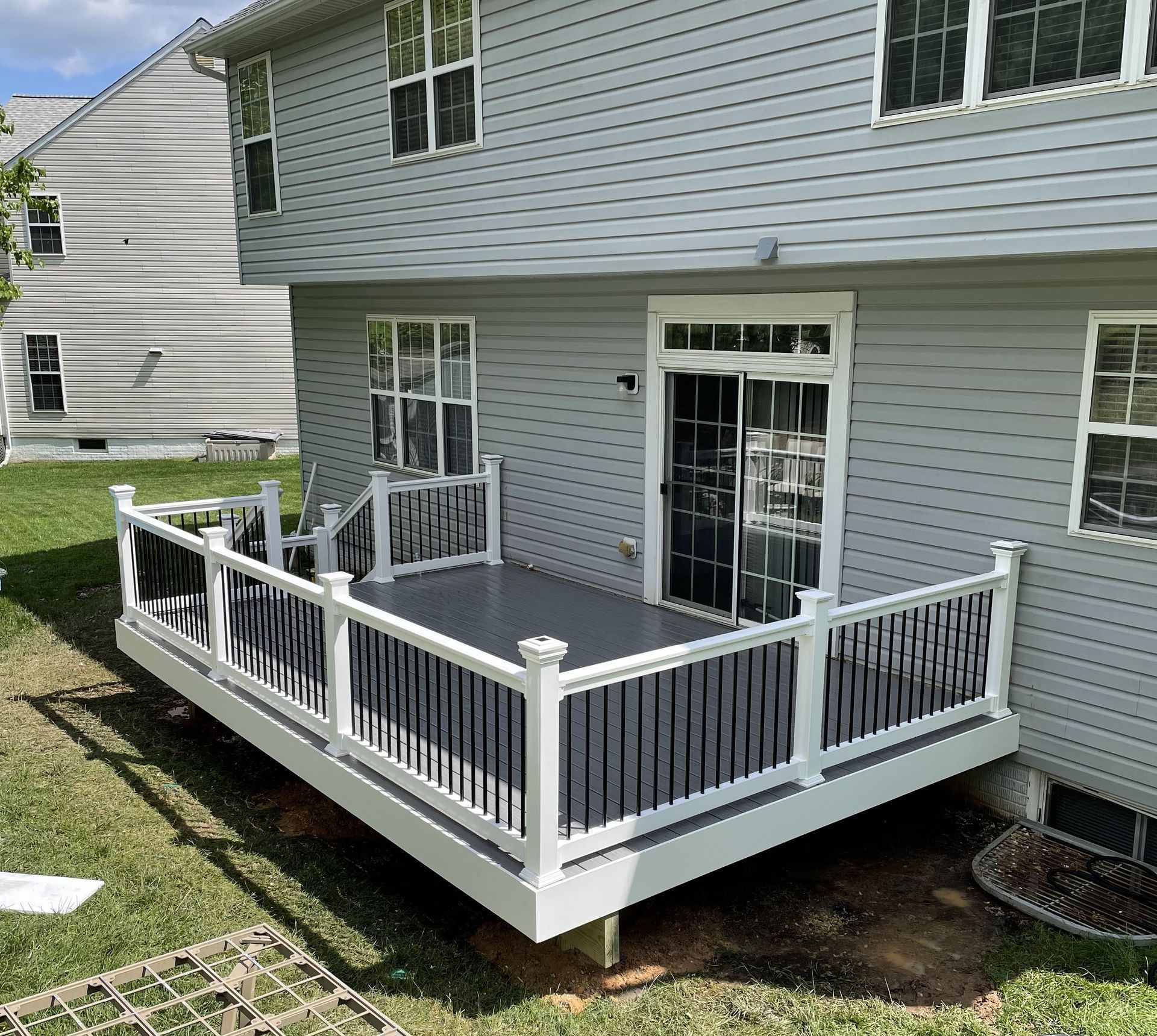 Backyard deck with white railings, dark gray flooring, and a sliding glass door.
