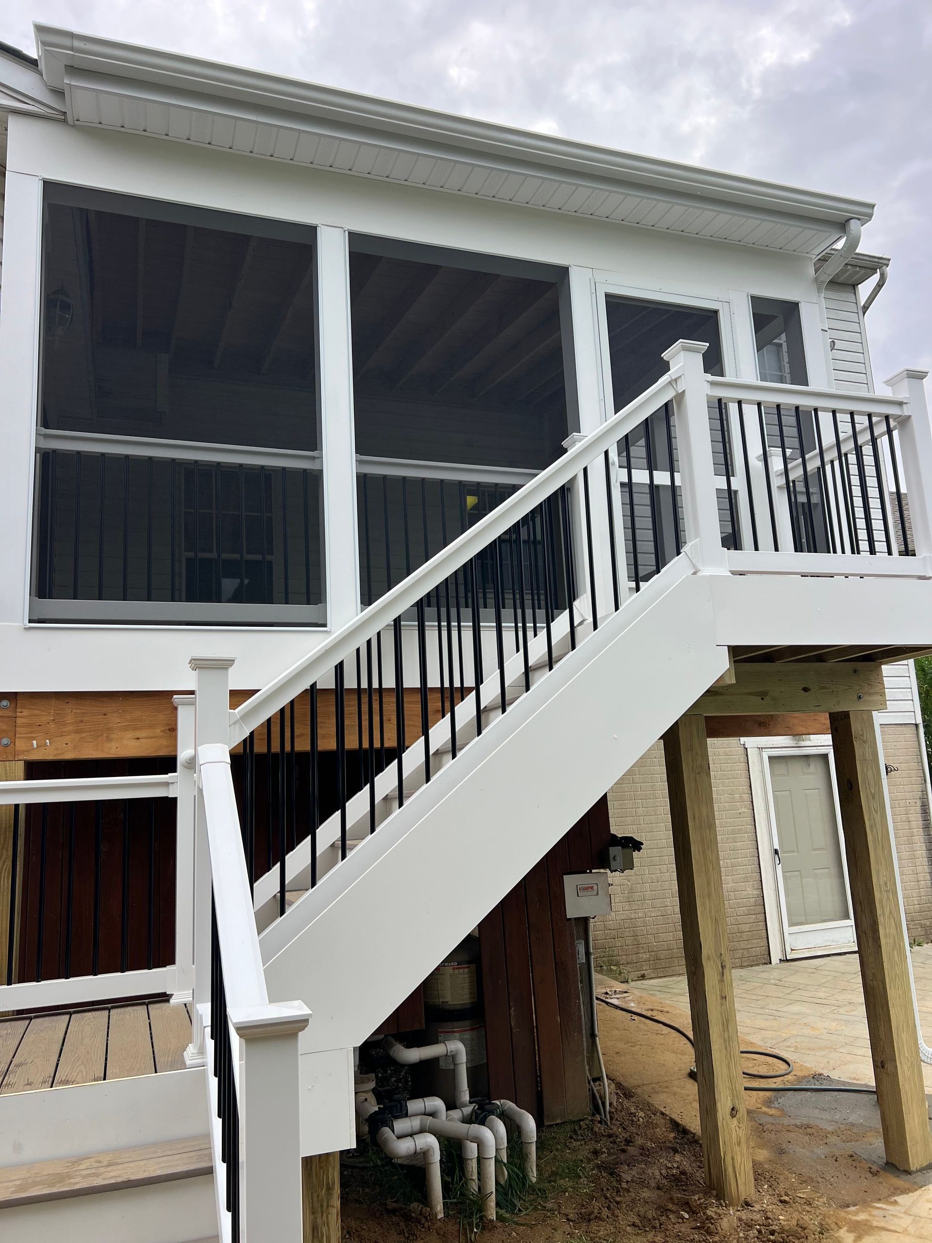 White deck with black railing and screened porch under cloudy sky.