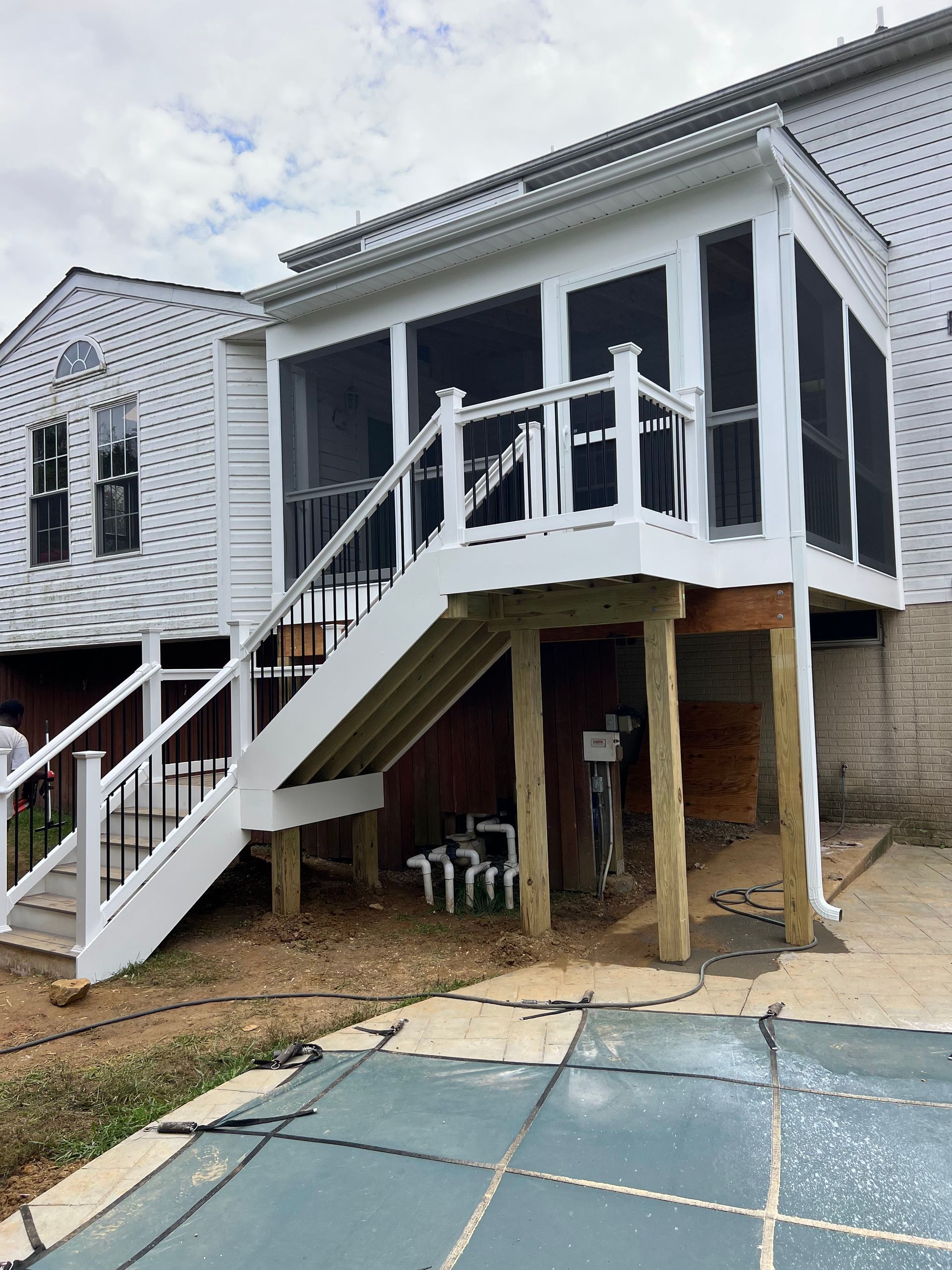 White screened porch with stairs attached to a house. Deck overlooks a pool.