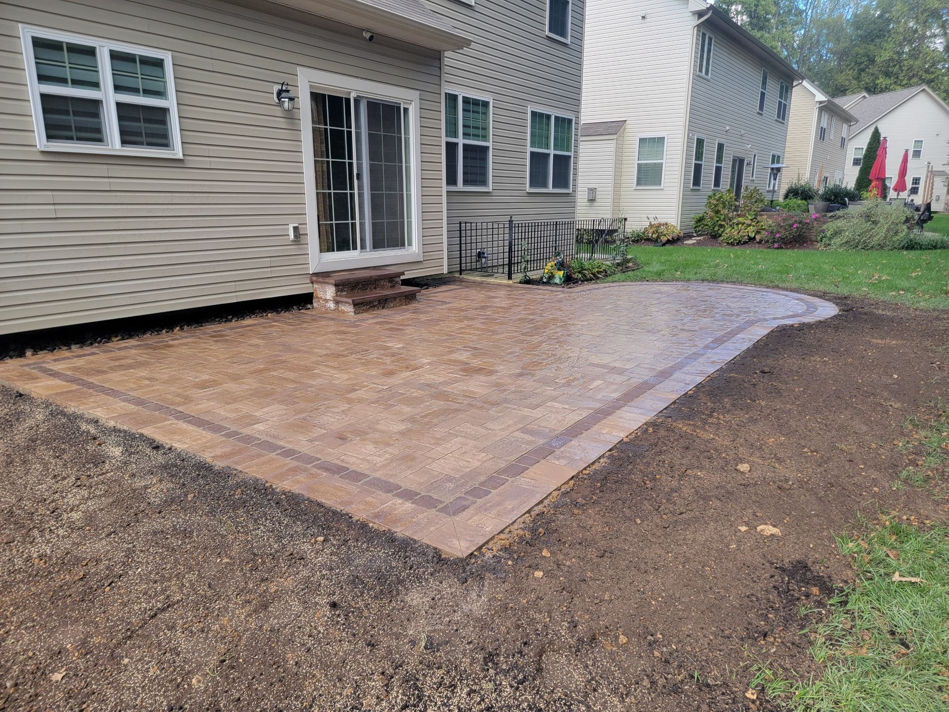 Paver patio with a dark border next to a beige house and green lawn.