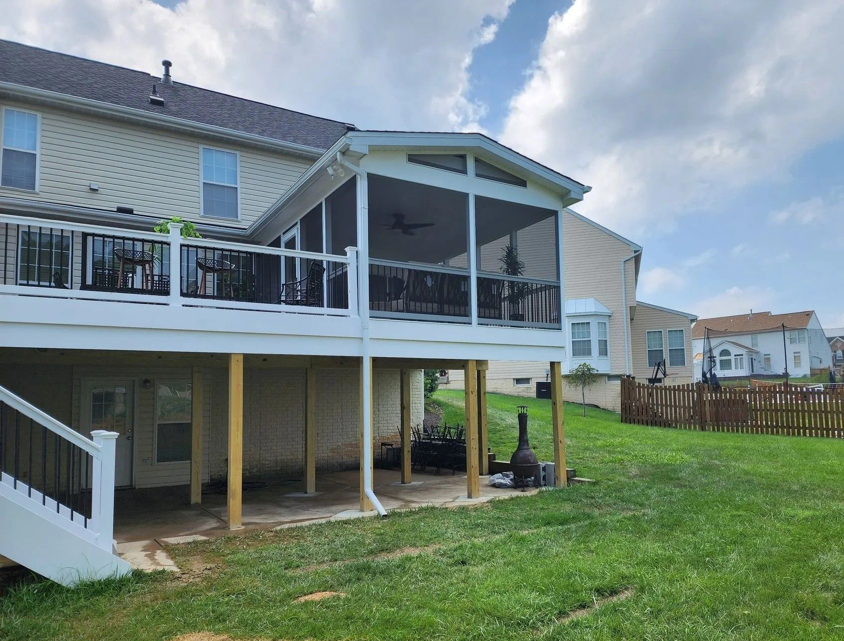 Backyard with elevated deck, screened-in porch, and fenced yard, sunny day.