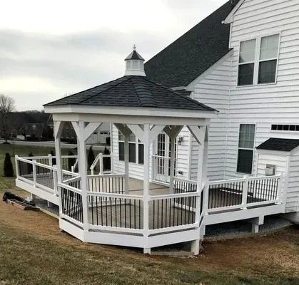White gazebo with black roof on a deck attached to a white house.