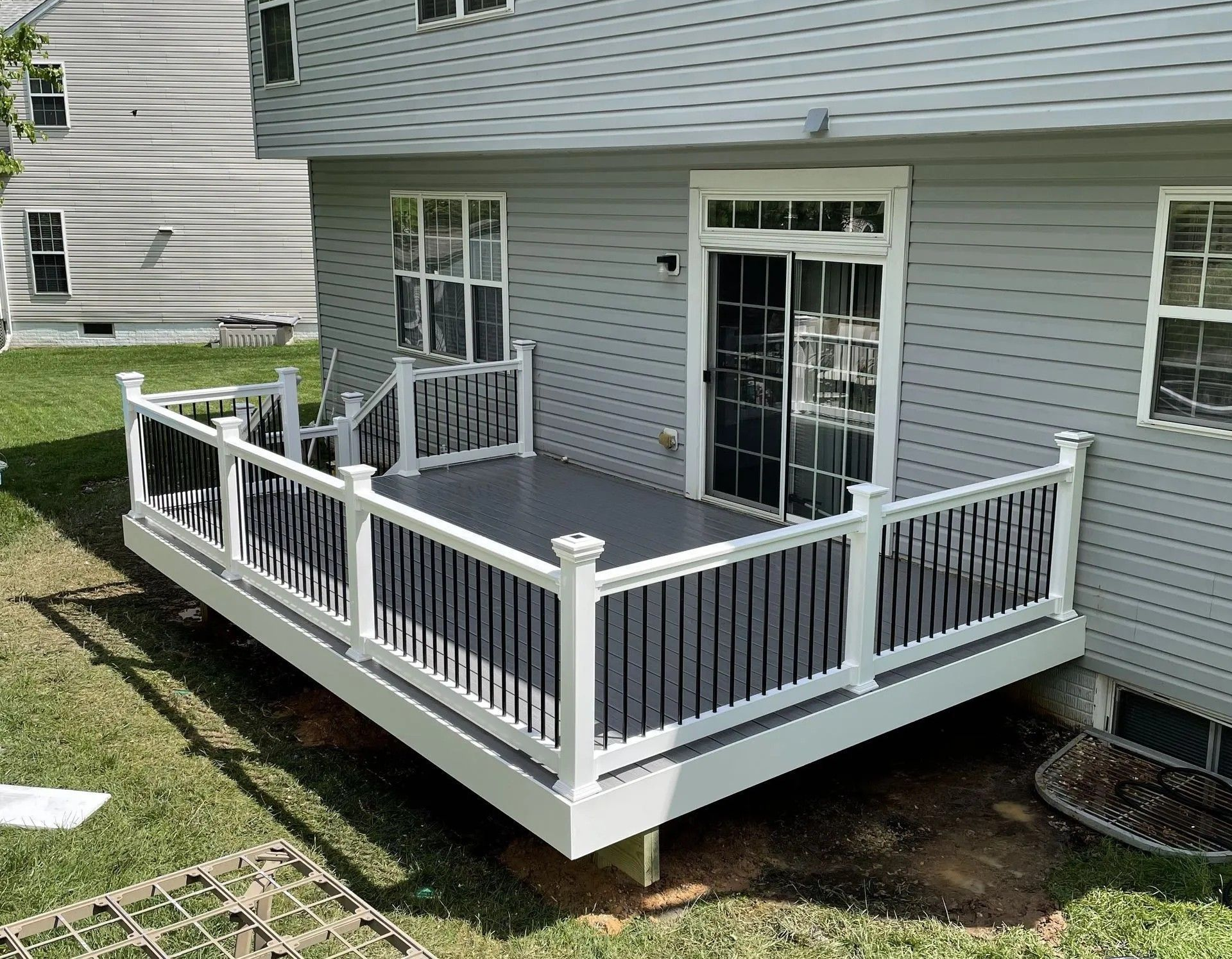 Gray house with small gray deck and white railings, in grassy backyard.