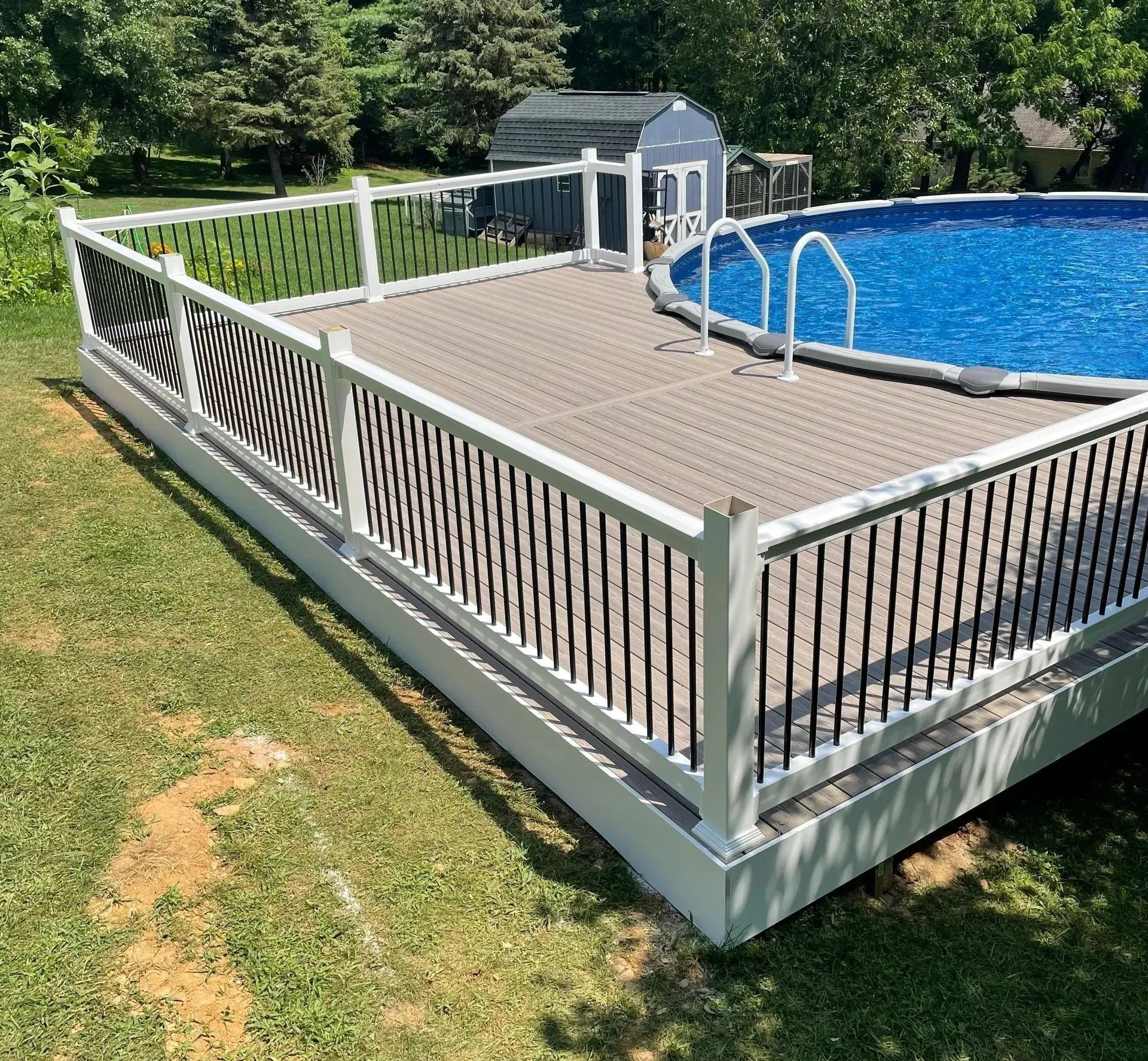 Above-ground pool with deck and white railing, set in a grassy yard, surrounded by trees.