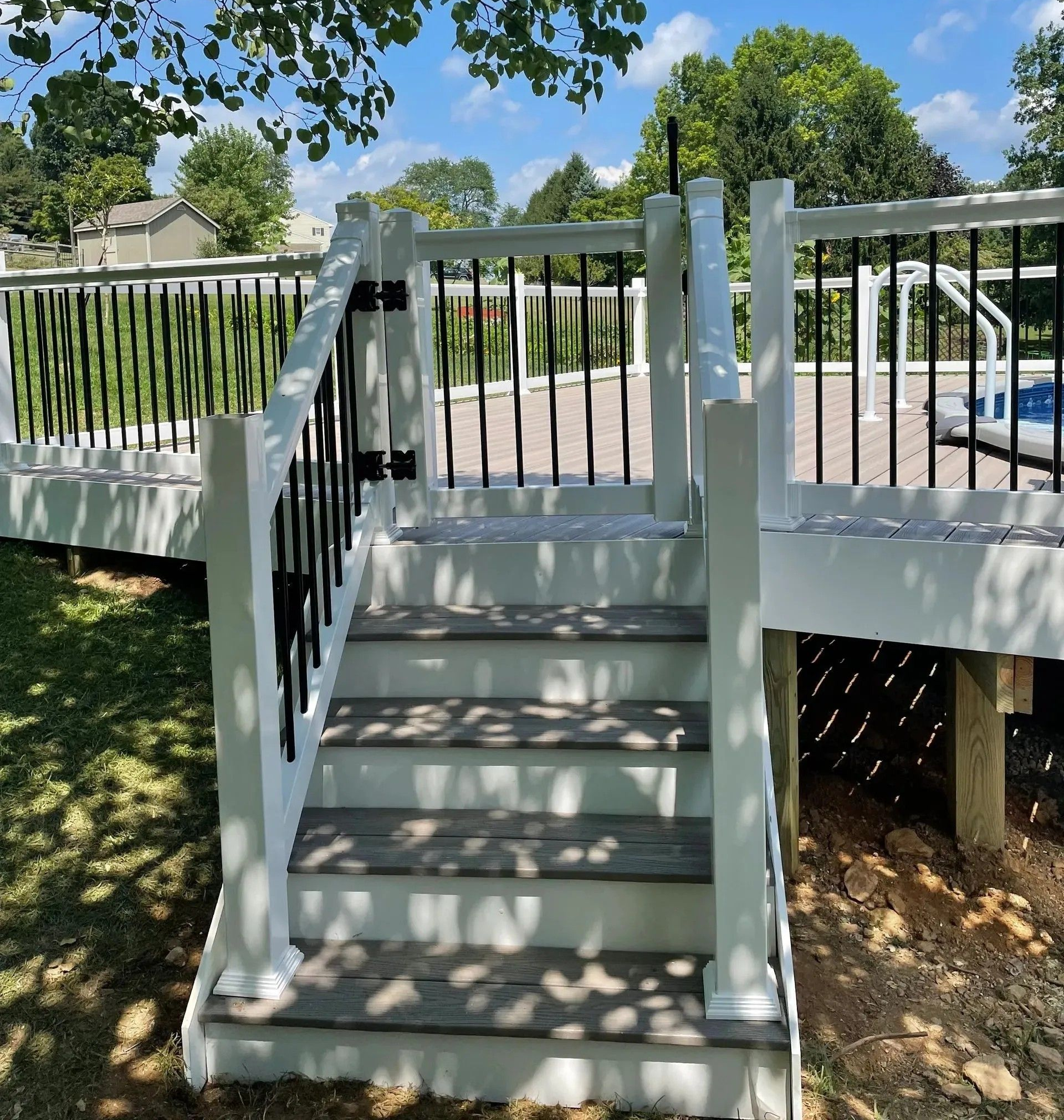 Stairs leading up to a white deck with a black railing. Sunny day.