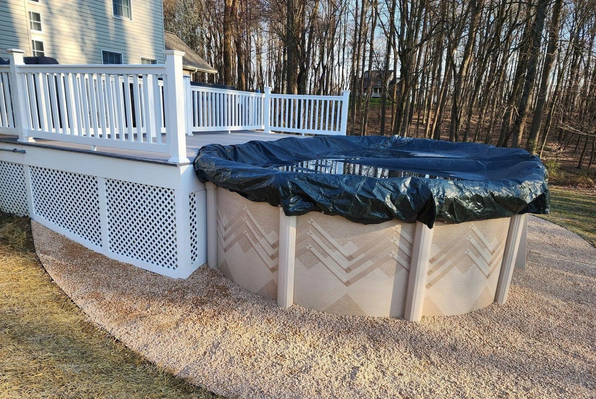 Above-ground pool covered with a black tarp next to a white deck on a bed of gravel.