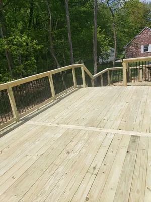 Wooden deck with black railing and steps leading up to a house surrounded by trees.