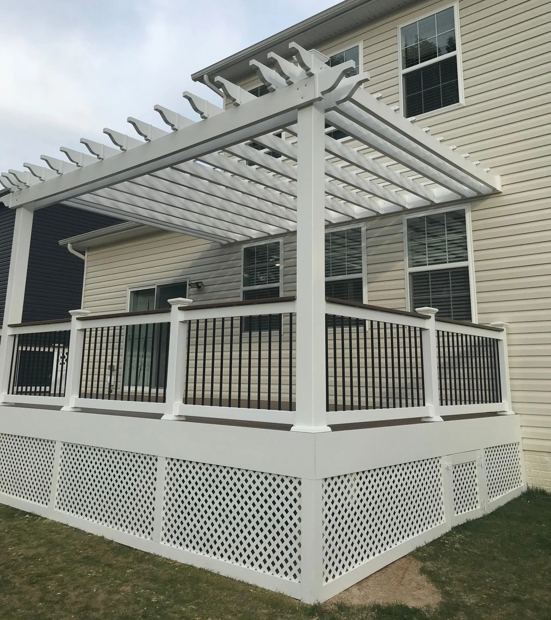 White pergola over a deck with white latticework skirt. The deck is attached to a beige house.
