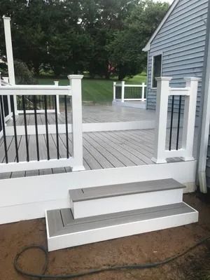 Newly built deck with gray composite decking, white railings, and steps, next to a house.