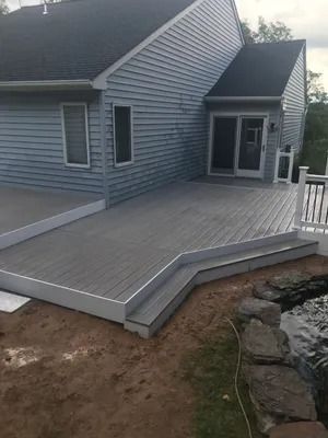 Gray composite deck with white trim, adjacent to a blue house and a small pond.