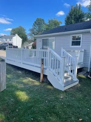 White deck with stairs attached to a light gray house, surrounded by a grassy yard.