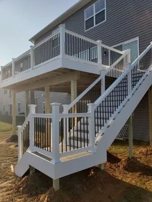 Two-level white deck with black railing, stairs to ground level, built into the back of a gray house.