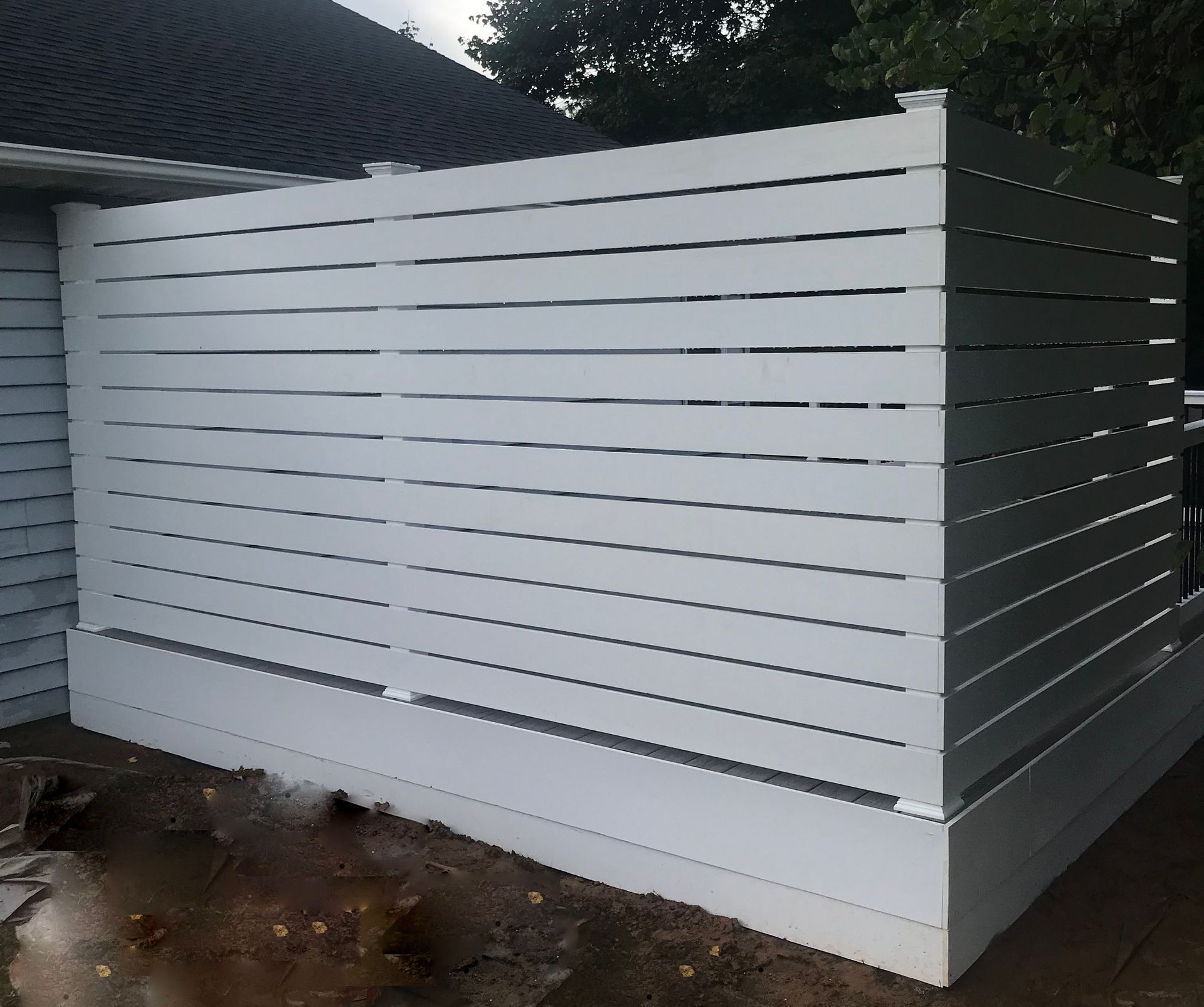 White horizontal slatted privacy fence adjacent to a house.