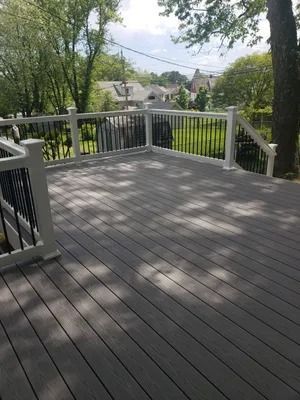 Gray composite deck with white railing, black spindles, and a tree in the backyard.