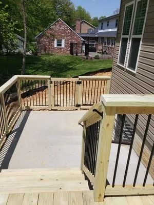 A wooden deck with a gate and black metal railings. Overlooks a yard with a brick building.