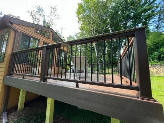 Brown deck with dark railing, attached to a house in a green yard.