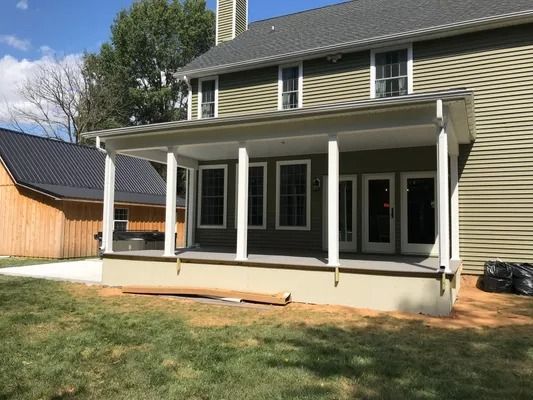 Backyard porch extension on a two-story house with white columns, green siding, and grassy lawn.