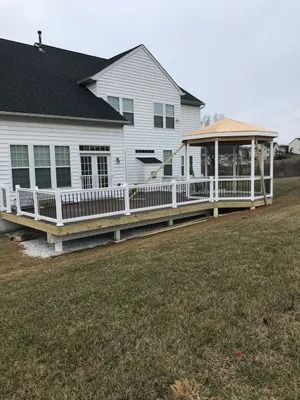 Back of a white house with a wooden deck, gazebo, and white railings. Overcast day, grassy yard.