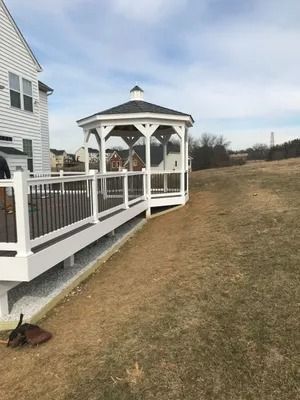 White gazebo on a deck attached to a house, overlooking a grassy yard.