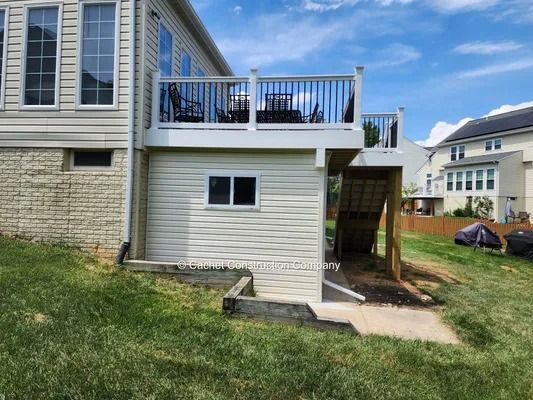 Backyard deck with stairs. Tan siding and railing. Overlooks green grass and other houses.