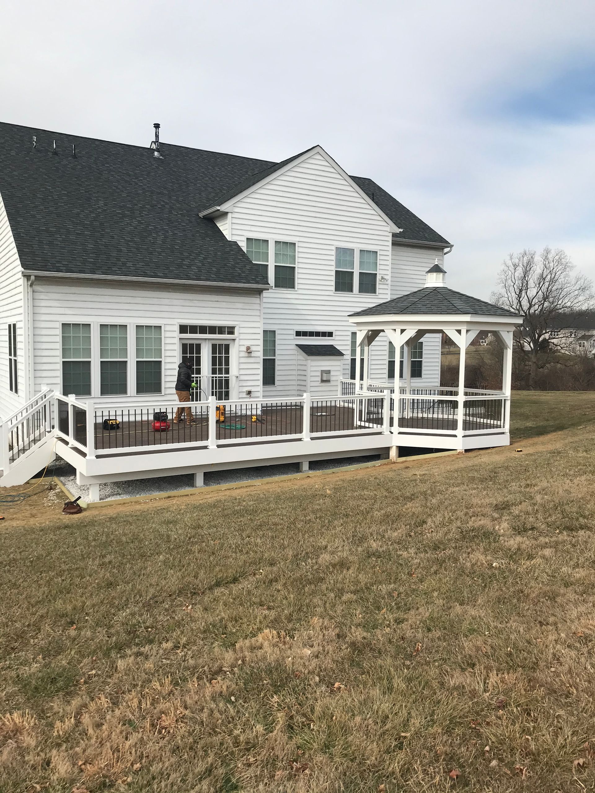 White house with a deck and gazebo; the house sits on a grassy hill on an overcast day.