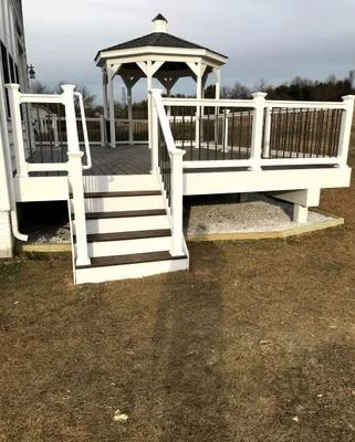 White deck and stairs with black railing leading to gazebo in a grassy area.