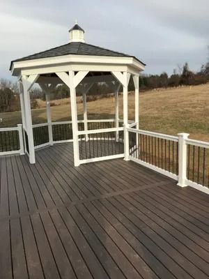 White gazebo on a gray deck with black railing overlooking a grassy field under a cloudy sky.