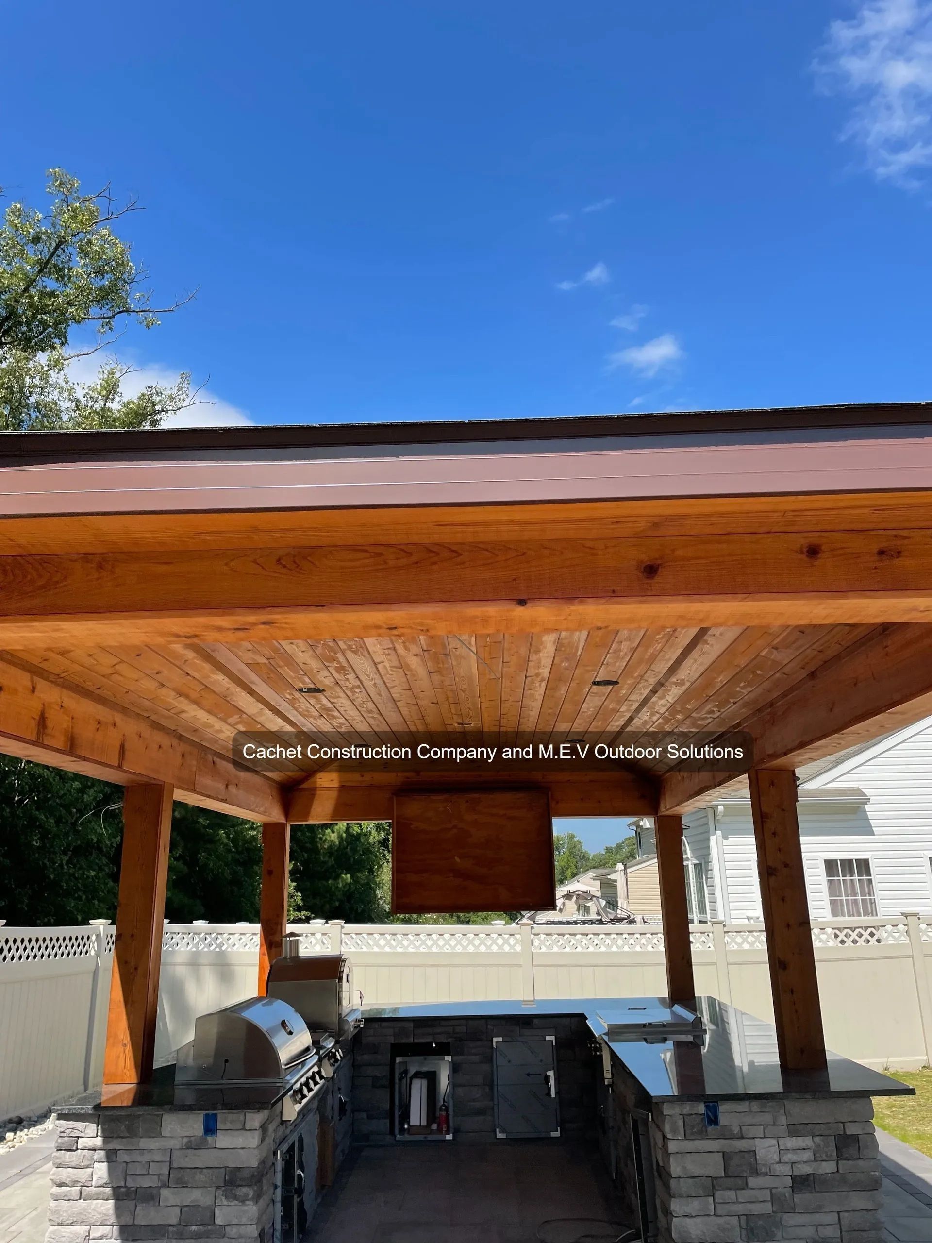 Outdoor kitchen with wooden ceiling, grill, countertops, and blue sky.