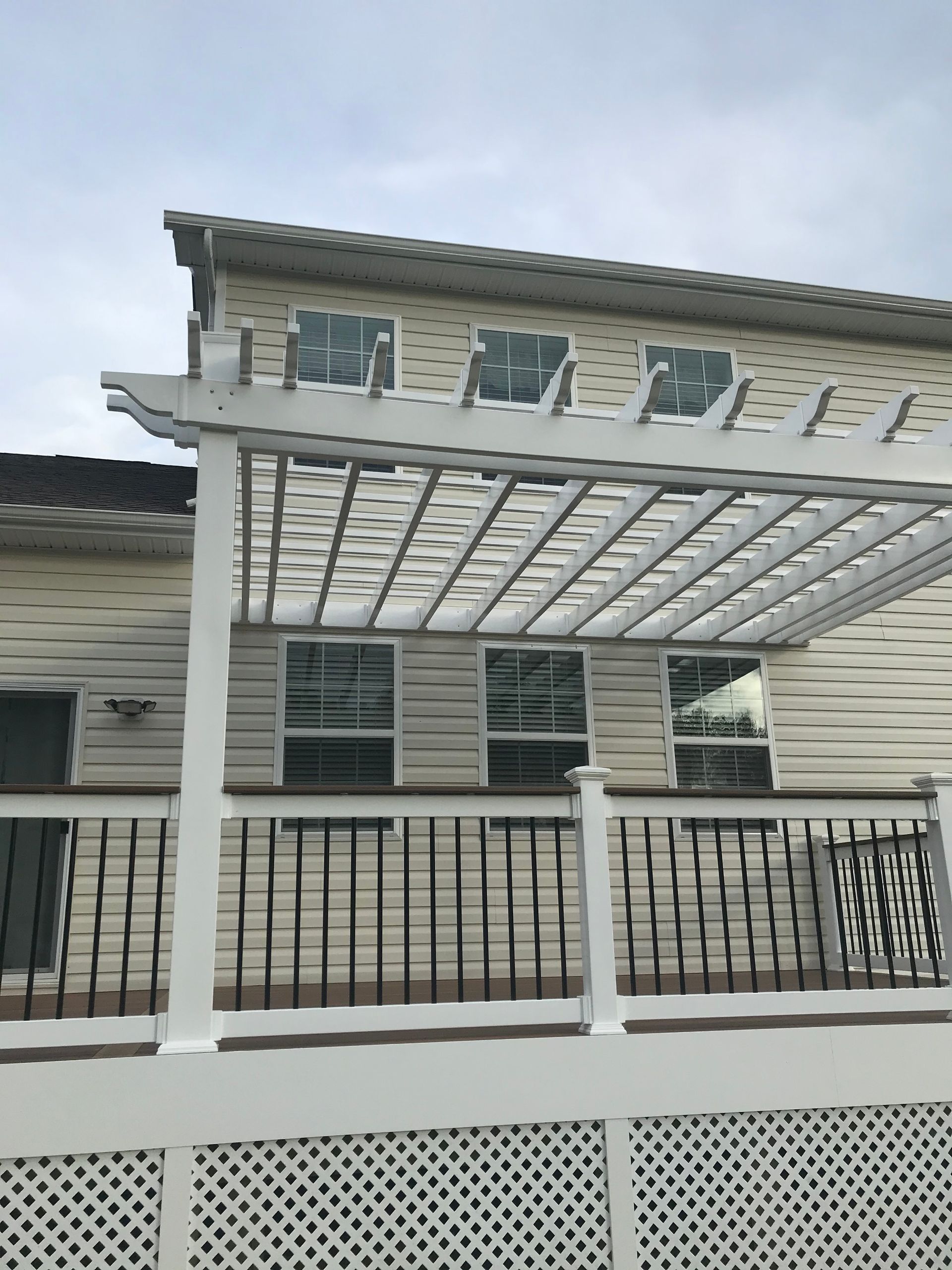 White pergola over deck, cream siding, black railing, and windows.