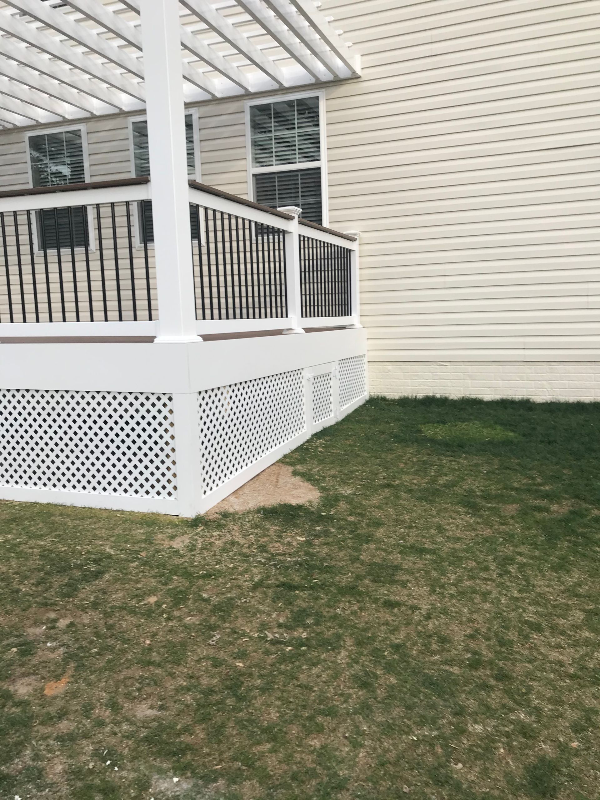 White deck with latticework skirting on a grassy lawn next to a light-colored house.